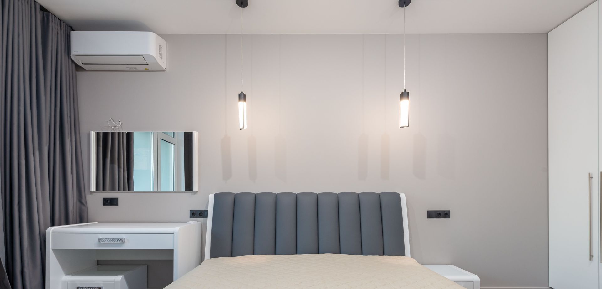Sleek minimalist bedroom design featuring a plush bed, pendant lighting, and modern furnishings.